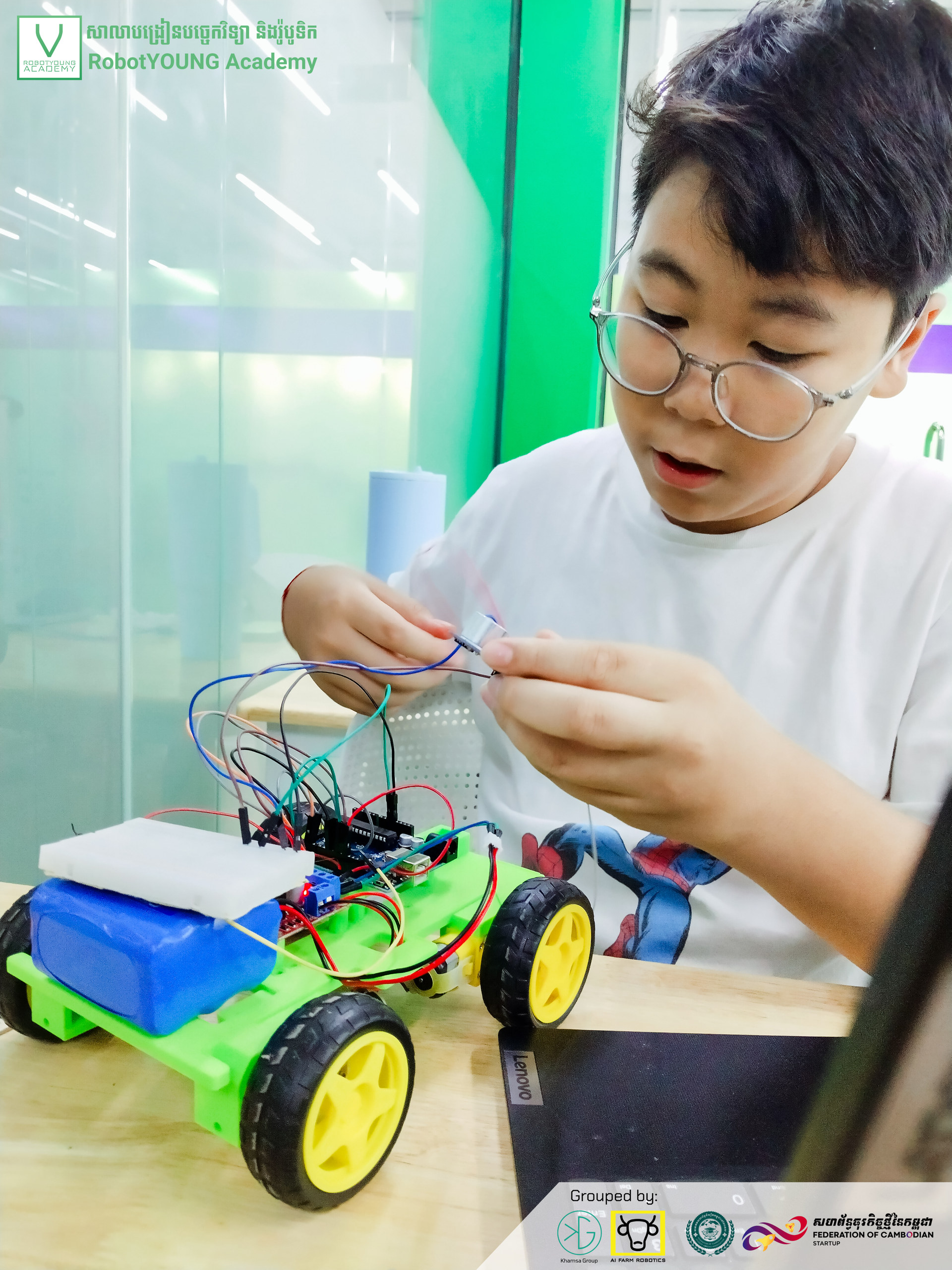 A student connecting wires on a green wheeled robot