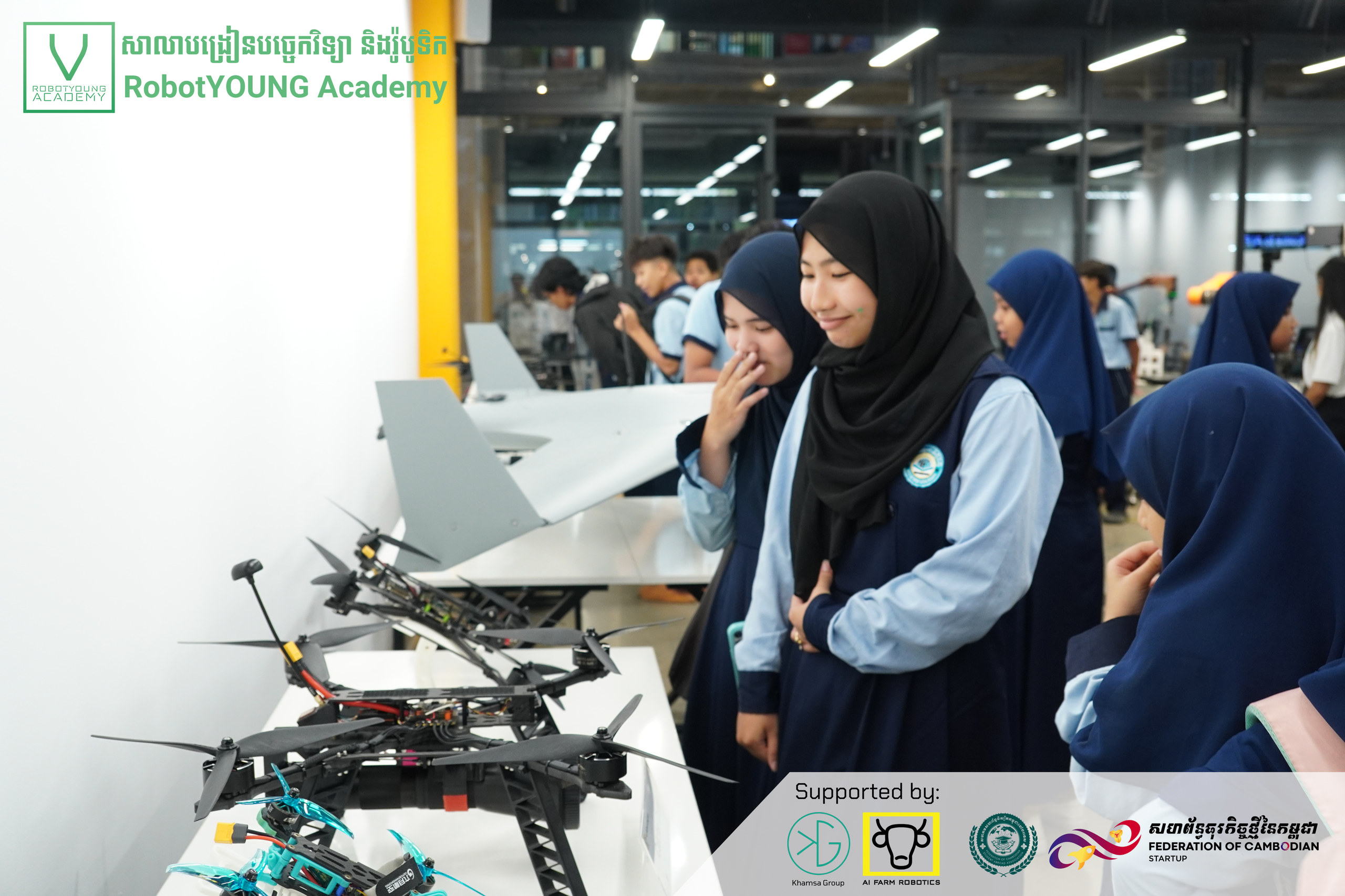 Students examining drones and a model aircraft displayed on an academy table