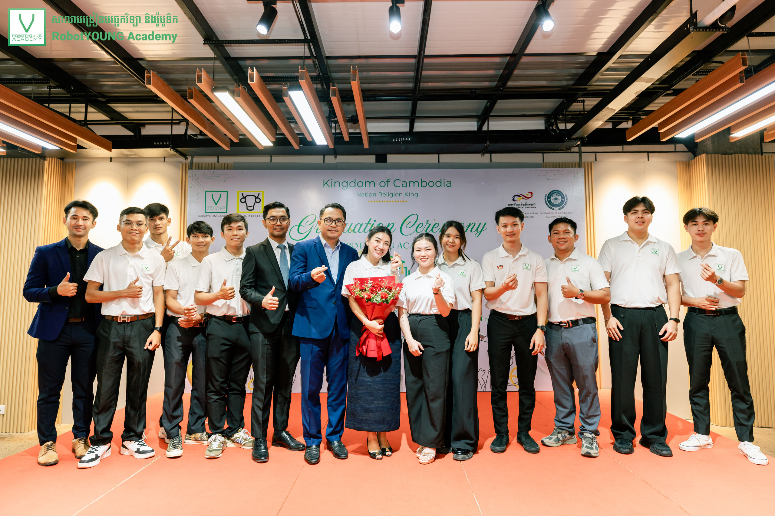 A group posing on stage in front of a RobotYOUNG Academy graduation banner