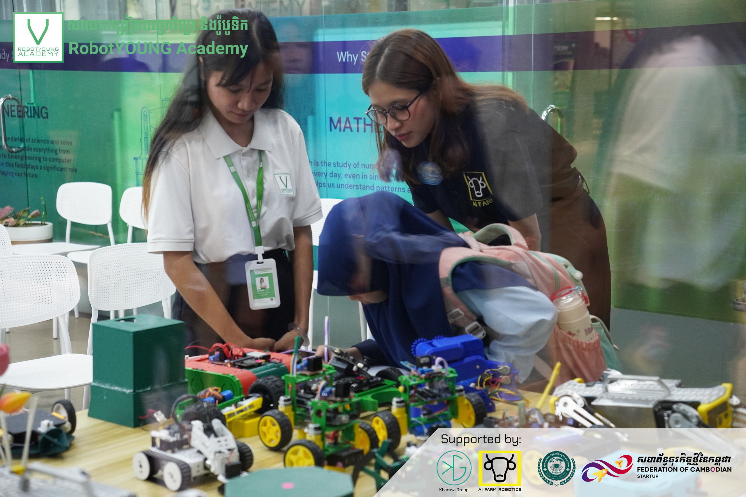 Visitors leaning over a table of wheeled robots with an academy guide