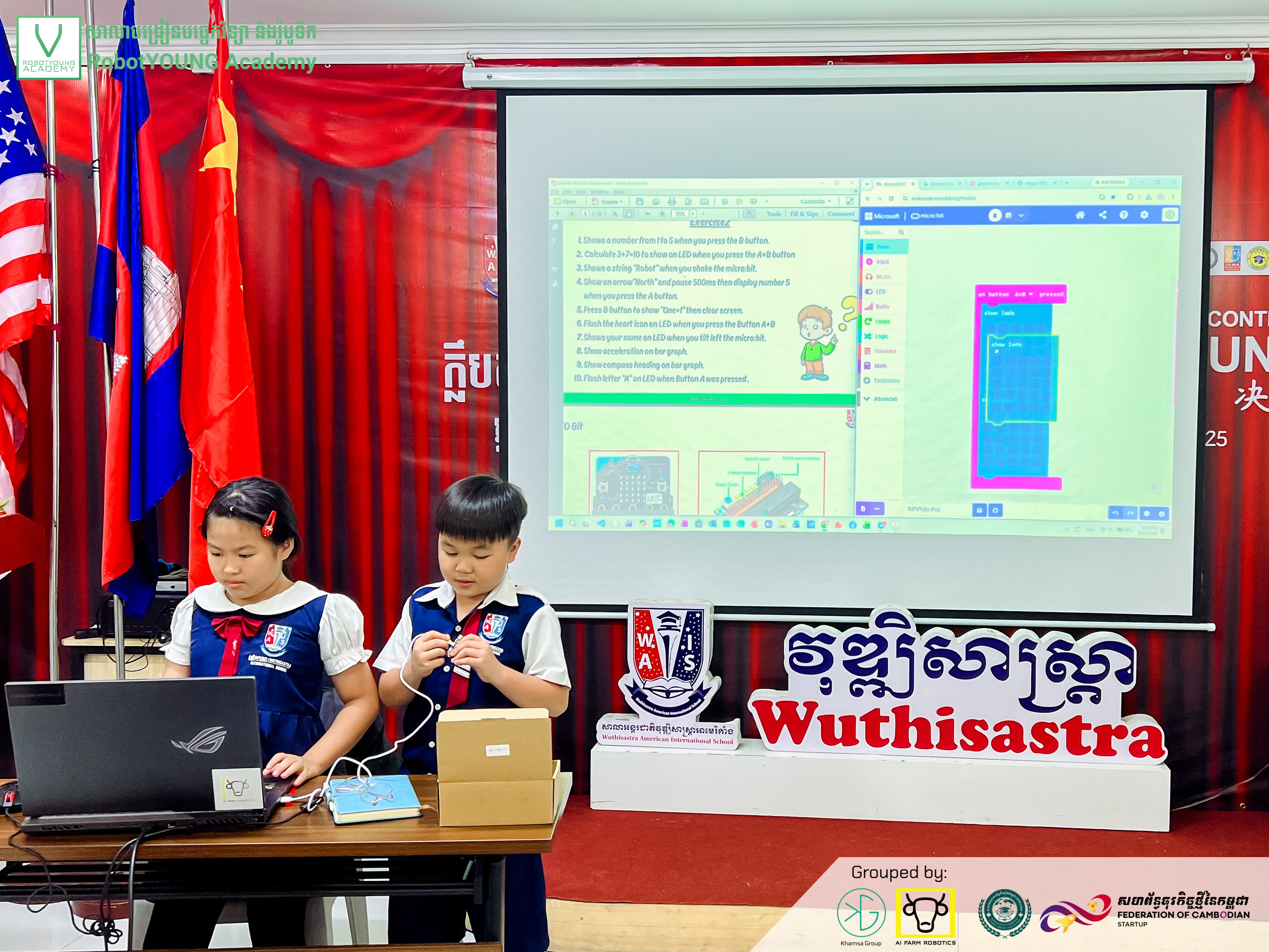 Two students presenting with a laptop and microphone in front of a projected programming screen