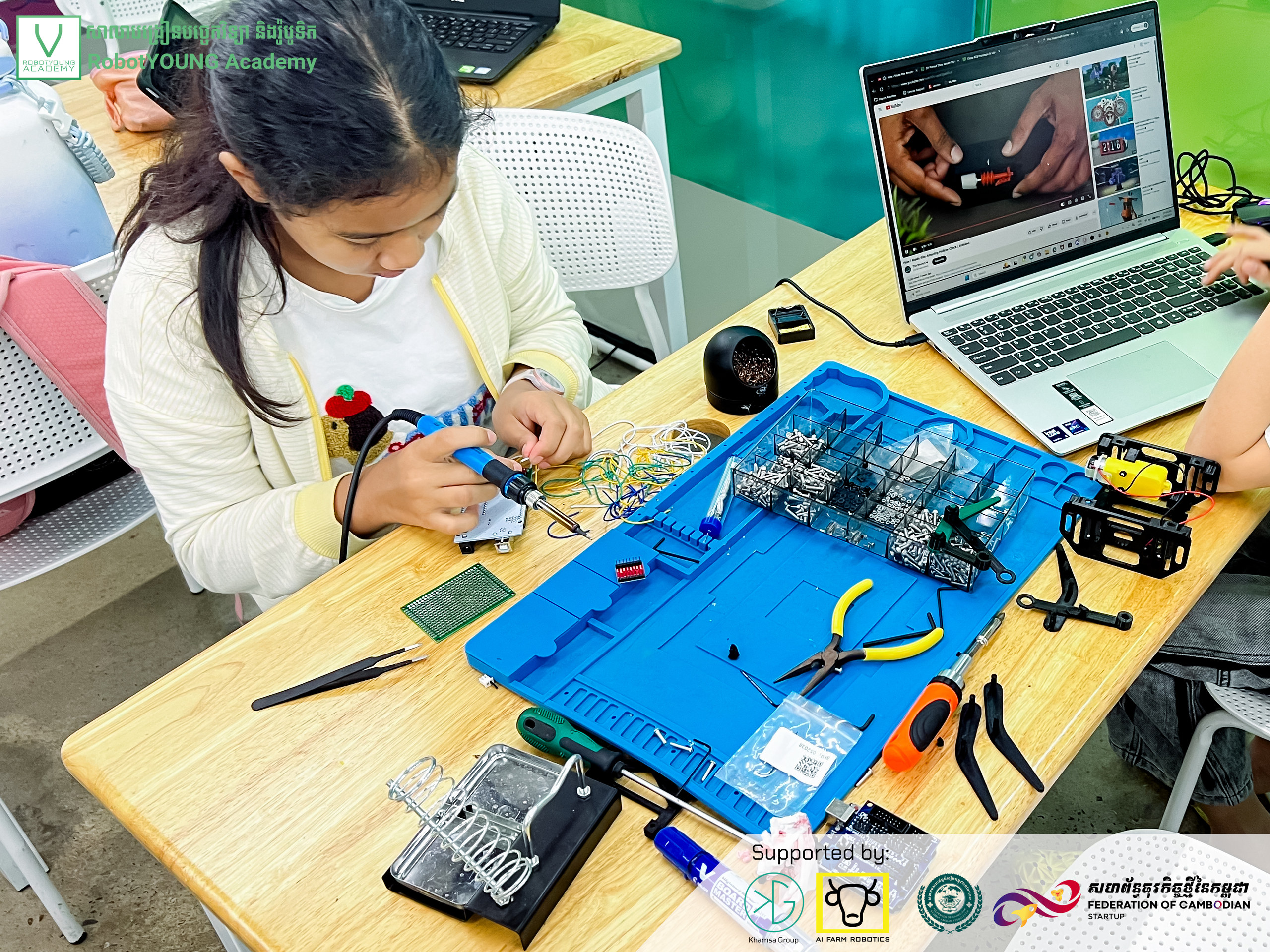 A learner working on a circuit board beside a laptop