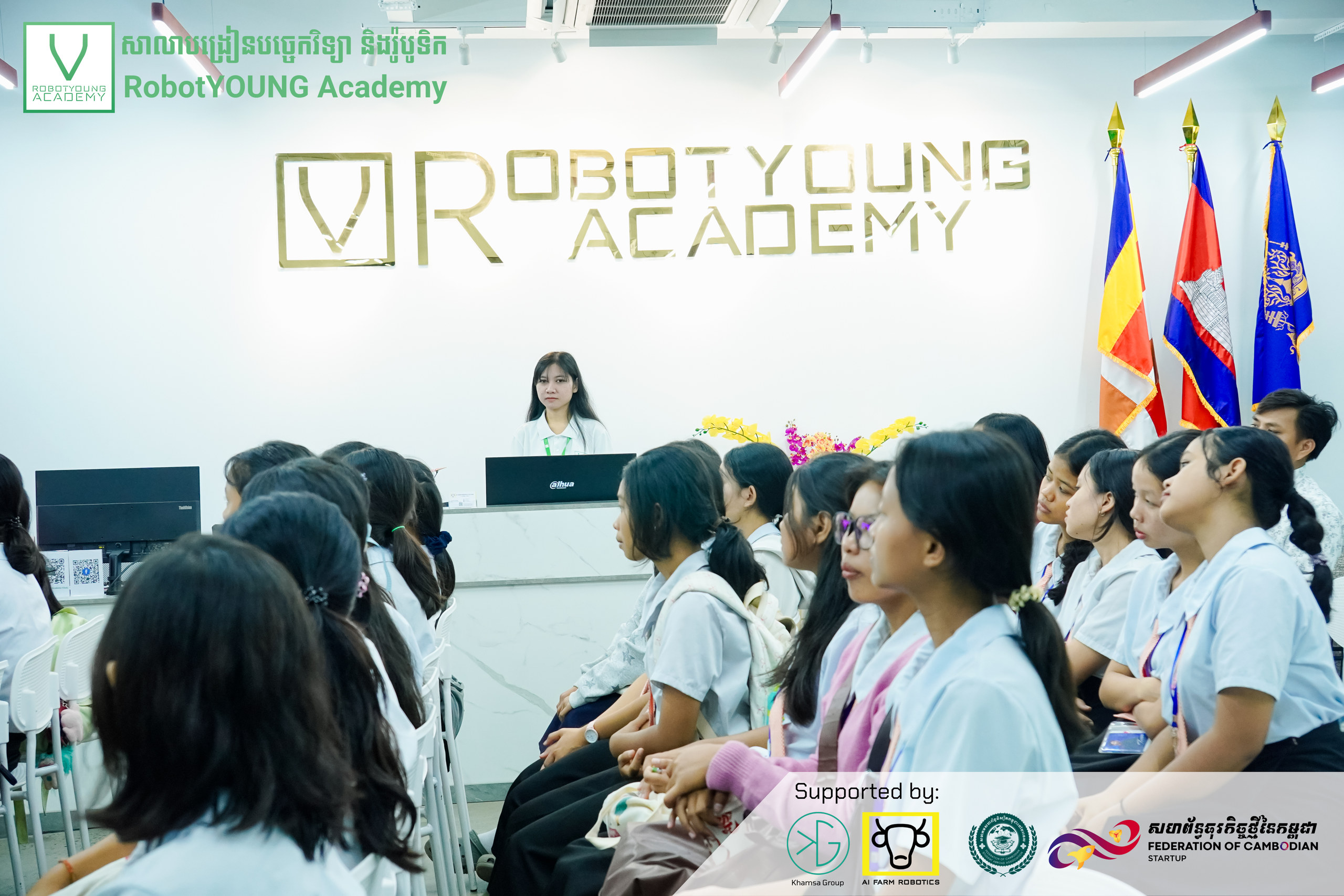 Uniformed students seated facing a presenter beneath the RobotYOUNG Academy wall sign