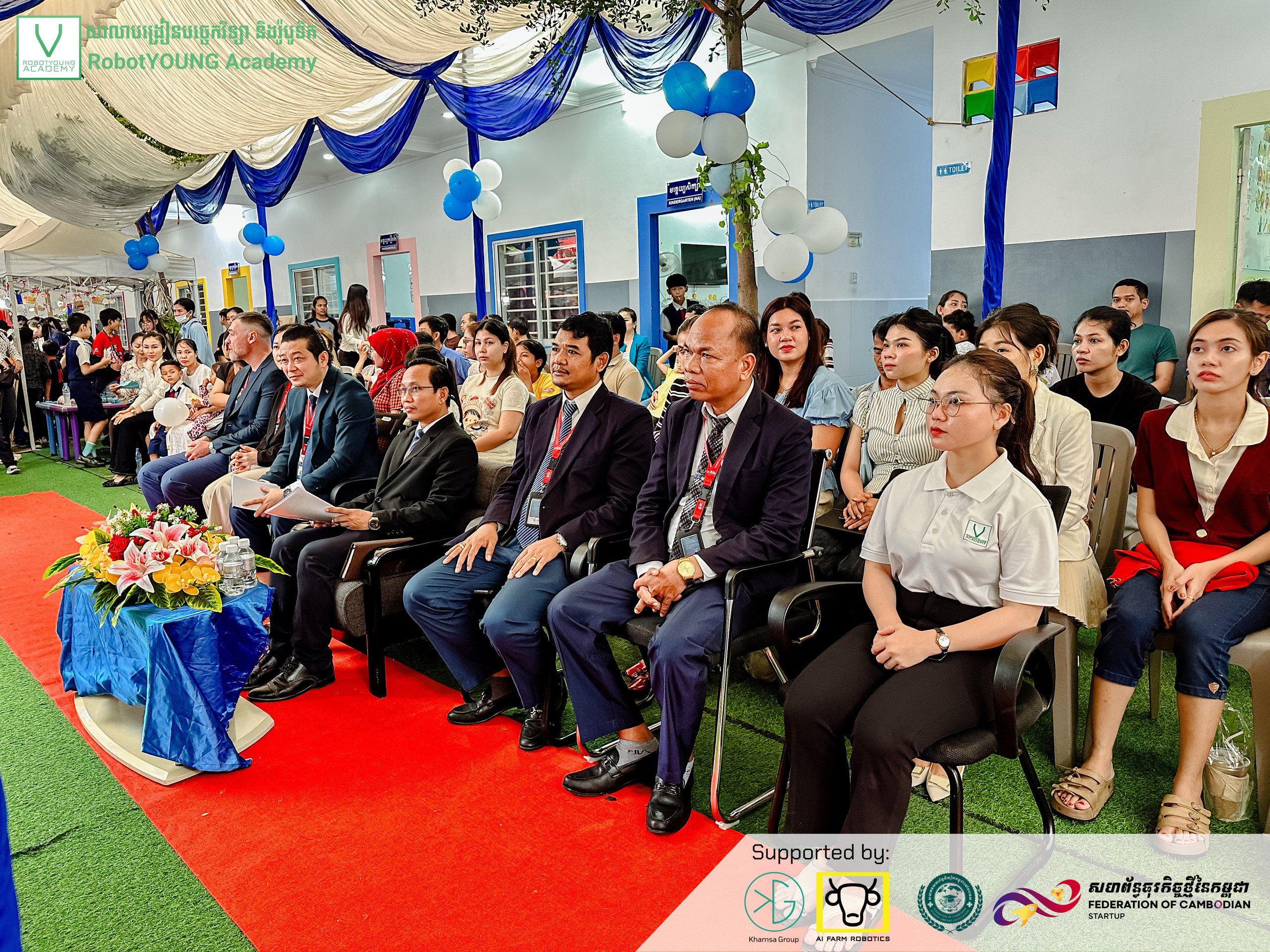 Guests seated in rows at an event with balloons and blue and white drapery