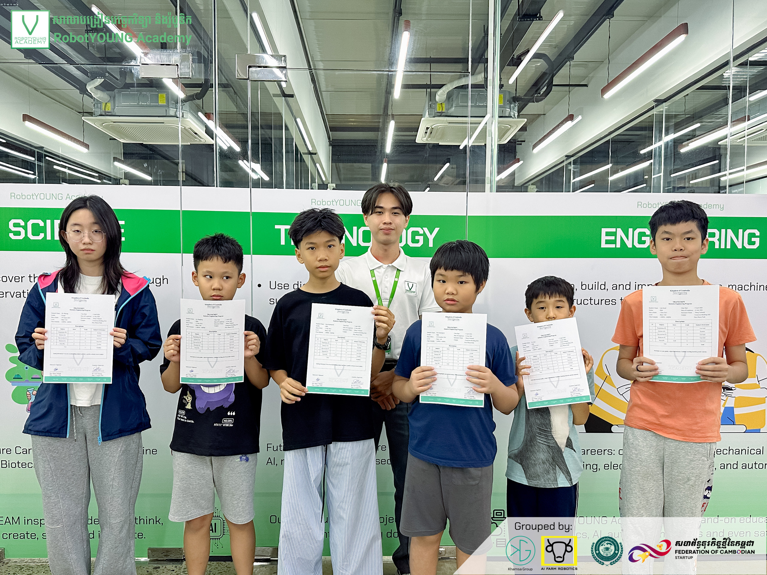 Children holding certificates alongside adults in front of a STEM display